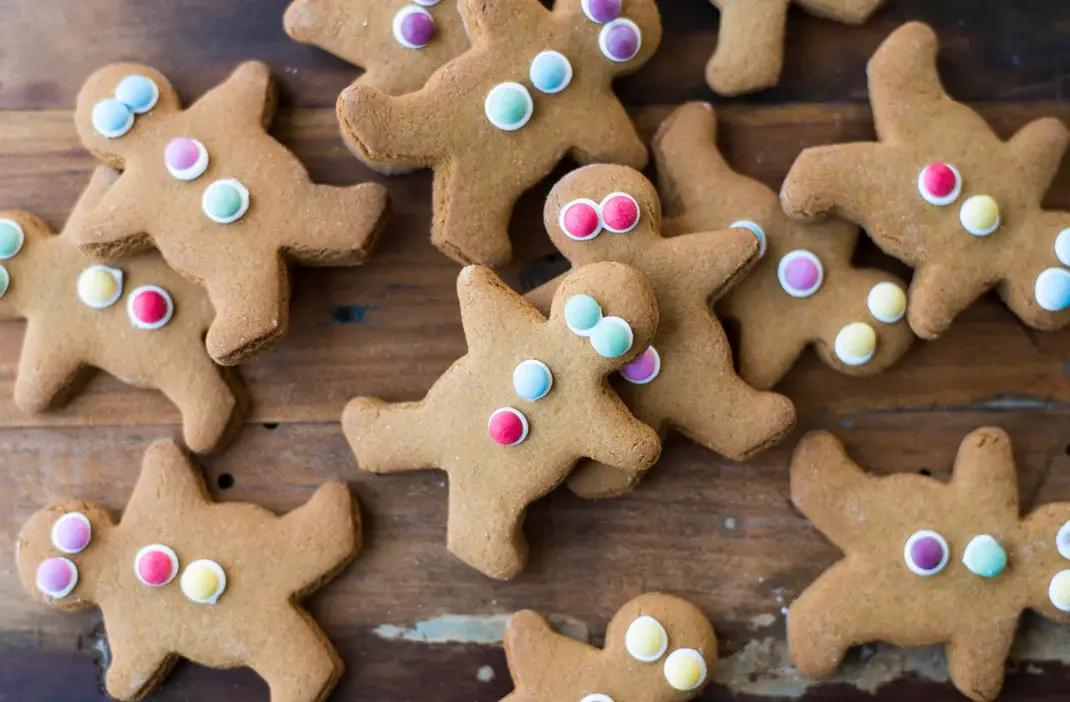 A pile of Molly Woppy gingerbread cookies shaped like gingerbread men, each decorated with colourful candy buttons.