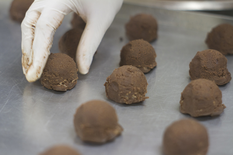 Hand shaping chocolate cookie dough scoops on baking tray — Molly Woppy artisan cookies crafted in New Zealand bakery.